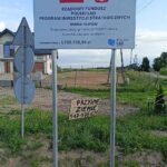 Tablica o rozbudowie drogi w gminie Filipów z funduszu Polski Ład. Pod nią odręczny napis na drewnie: Przyjmę ziemię